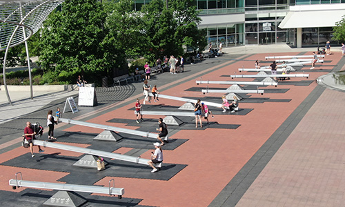 Impulse Large seesaws on a long brick path with several people playing on them.