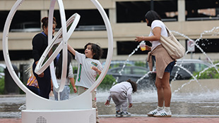 A child playing with a gyroscope with a water fountain spraing in the background.