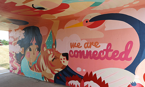 A painted mural of a woman holding onto a bear and the words "we are connected" are painted in pink.