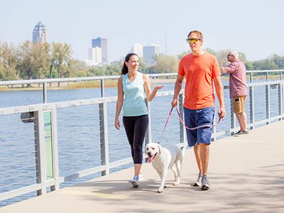 Gray's Lake A couple walking across a bridge, walking a dog. The Downtown Des Moines skyline is in the background