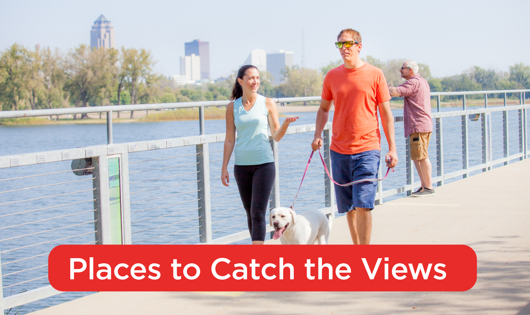 A man and a woman walking a dog on a bridge over water with the Des Moines skyline in the background. Text at the bottom of the photo reads, "Places to Catch the Views"