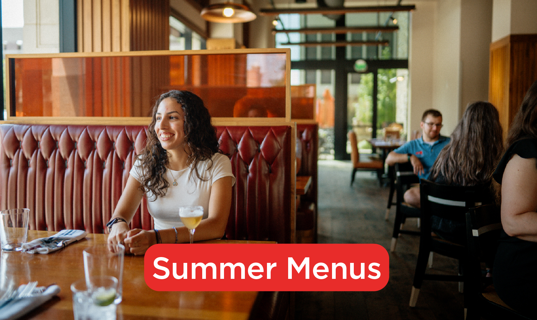 A woman sitting at a booth, smiling with a drink in front of her. The words "Summer Menus" are in text.
