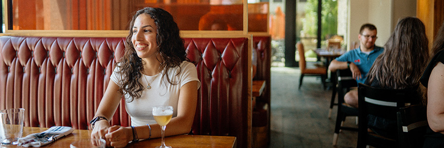 A woman sitting in a booth, enjoying a drink and looking out the window.