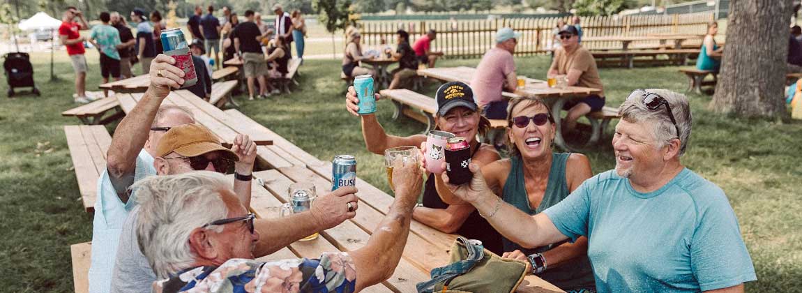 people hold up drinks to cheers at picnic table