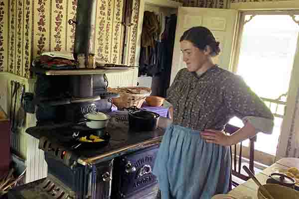 A woman dressed in 1900's clothing, preparing dinner