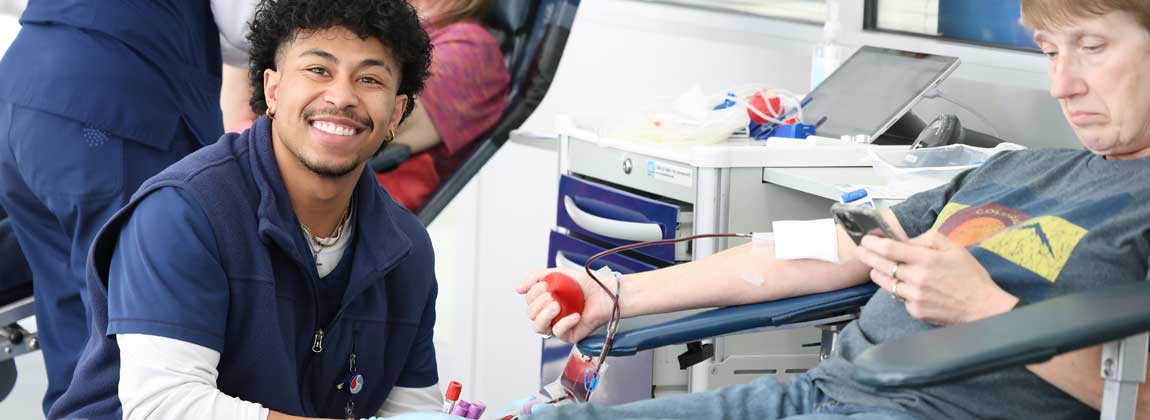 woman gives blood while man smiles at camera