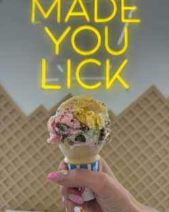 a hand holding an ice cream cone below a sign
