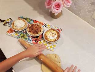 hands rolling dough with a rolling pies with three small pies on the counter