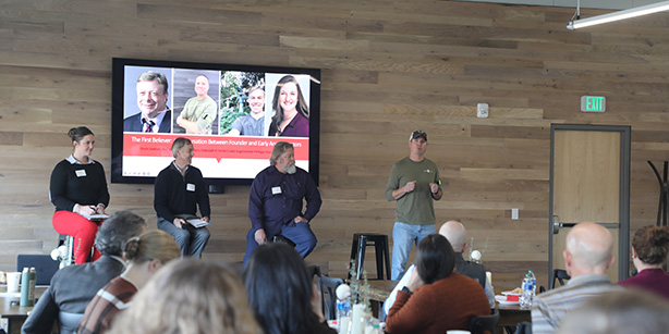 Four people on stage talking to a crowd of people.
