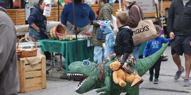 A child in a dinosaur costume on a street with vendors