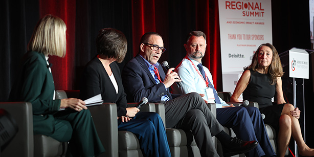 Five people sitting on chairs and one talking into a microphone