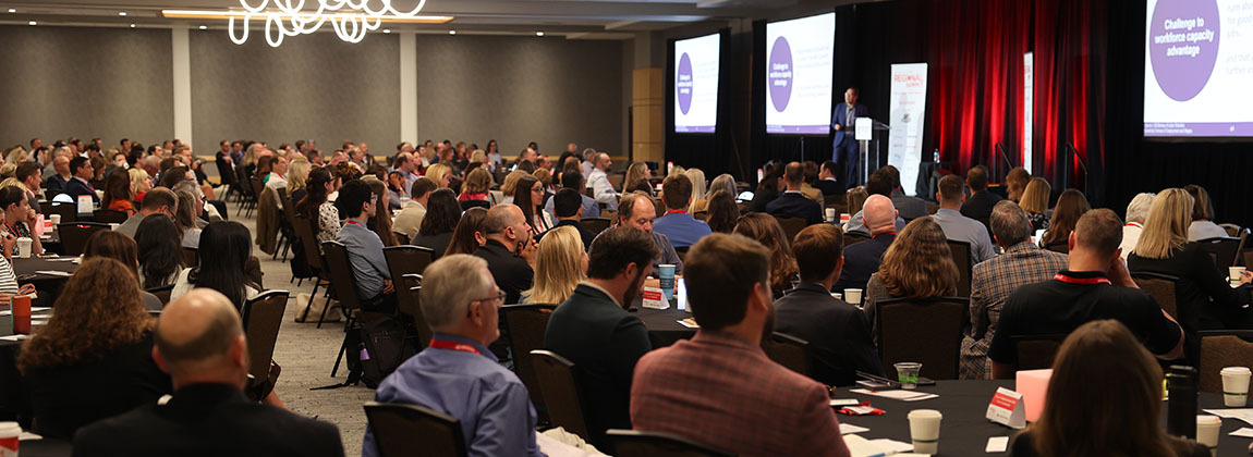 A large room filled with over 200 people watching someone on a stage